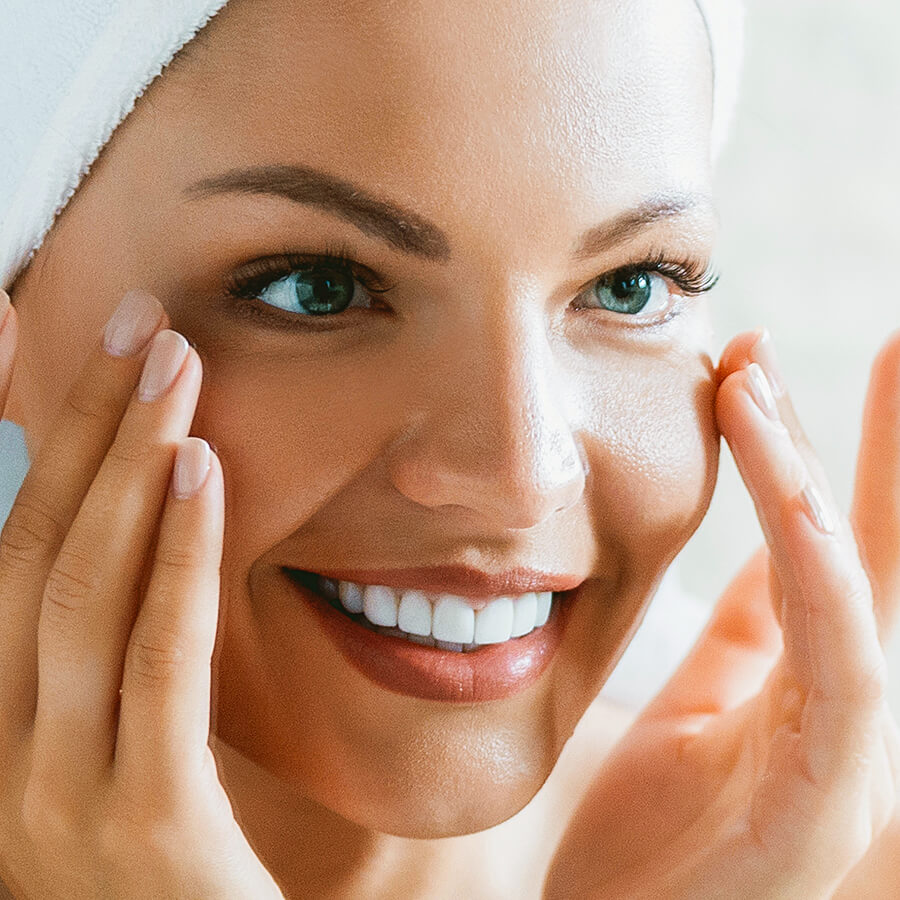 Woman touching face, looking in mirror. Noticing difference Hyaluronic Acid makes on her face. Hyalogic